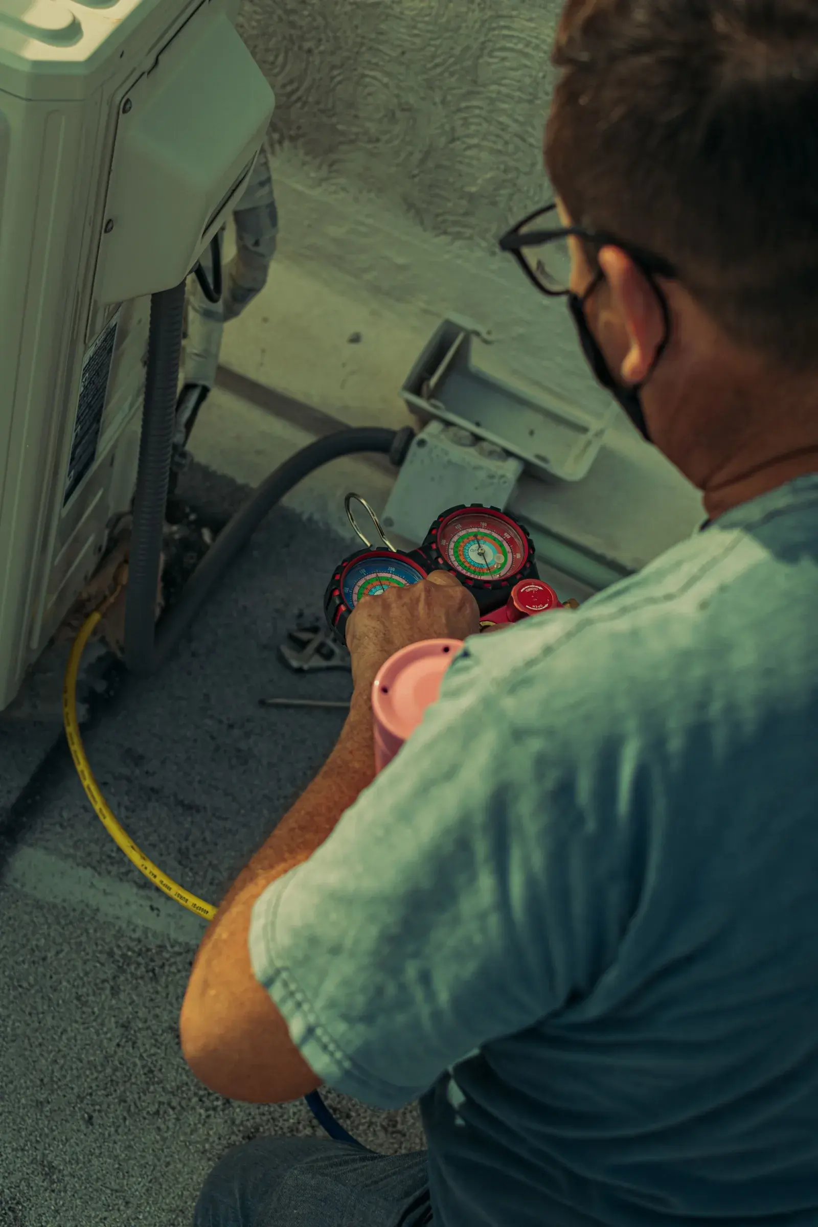 HVAC technician using refrigerant gauges during an air conditioner tune-up on a residential condenser