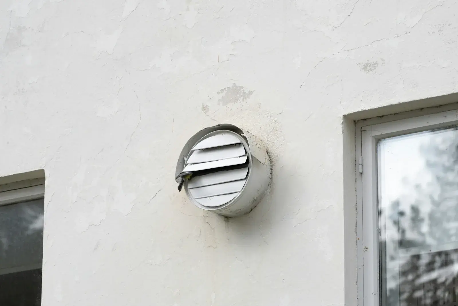 Round dryer vent cap mounted on a white stucco exterior wall